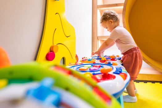 Toddler playing with interactive toy table featuring lights, sounds, and shapes in a play area
