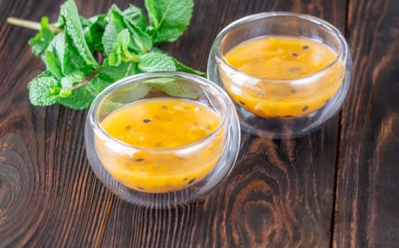 Two glass bowls filled with passion fruit pulp and fresh mint on a dark rustic wooden background