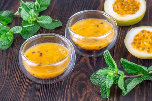 Two glass bowls filled with passion fruit pulp and fresh mint on a dark rustic wooden background
