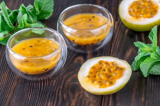 Two glass bowls filled with passion fruit pulp and fresh mint on a dark rustic wooden background