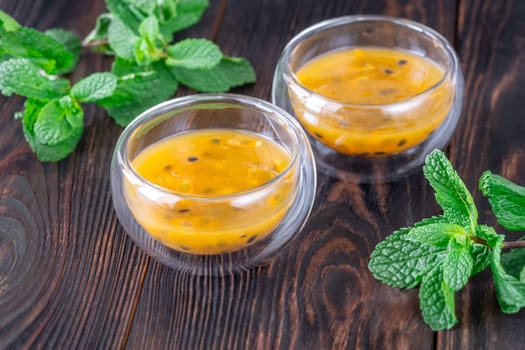 Two glass bowls filled with passion fruit pulp and fresh mint on a dark rustic wooden background
