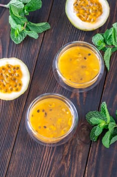 Two glass bowls filled with passion fruit pulp and fresh mint on a dark rustic wooden background