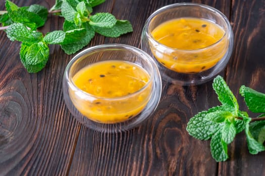Two glass bowls filled with passion fruit pulp and fresh mint on a dark rustic wooden background