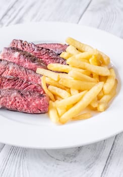 Sliced medium-rare ribeye steak with golden french fries served on a white plate on a wooden table
