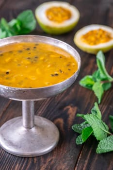 Passion fruit pulp, halved fruit, and fresh mint in a rustic metal vase on a dark wooden background