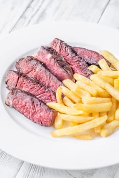 Sliced medium-rare ribeye steak with golden french fries served on a white plate on a wooden table