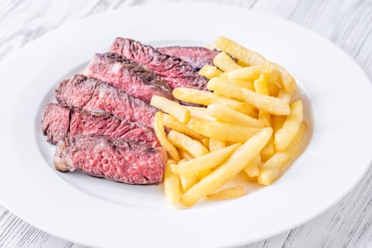Sliced medium-rare ribeye steak with golden french fries served on a white plate on a wooden table