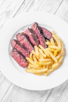 Sliced medium-rare ribeye steak with golden french fries served on a white plate on a wooden table