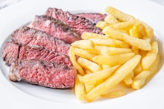Sliced medium-rare ribeye steak with golden french fries served on a white plate on a wooden table