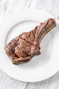 Whole grilled medium-rare cowboy steak served on a white plate on a white wooden table