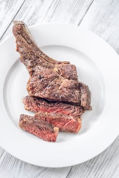 Sliced grilled medium-rare cowboy steak served on a white plate atop a white wooden table