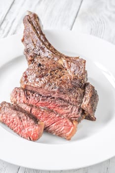 Sliced grilled medium-rare cowboy steak served on a white plate atop a white wooden table