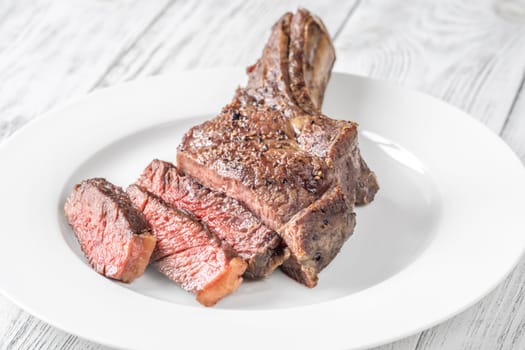 Sliced grilled medium-rare cowboy steak served on a white plate atop a white wooden table