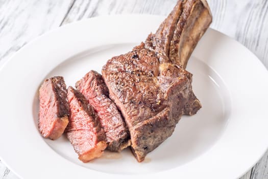 Sliced grilled medium-rare cowboy steak served on a white plate atop a white wooden table