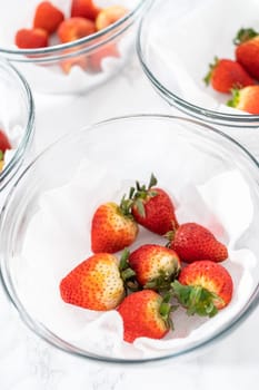 Bright red strawberries, interspersed with signs of mold, rest in a glass bowl lined with a paper towel on a white napkin, indicating improper storage techniques.