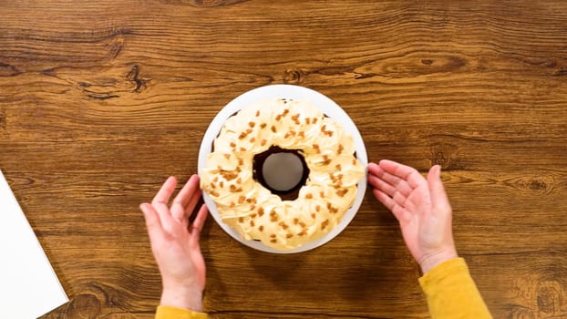 Flat lay. Carefully placing the gingerbread bundt cake, adorned with salted caramel frosting and gingerbread sprinkles, into a white paper bundt cake box with a clear window for gifting.