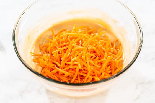 In a large glass bowl, the ingredients are expertly mixed to create the batter for baking the scrumptious Carrot Bundt Cake.