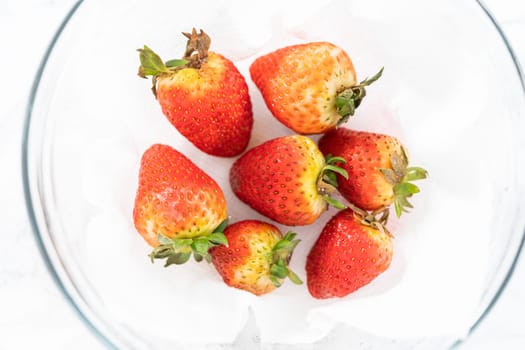 Freshly washed and dried strawberries are carefully arranged in a glass bowl lined with paper towel, ready for snacking or further use.