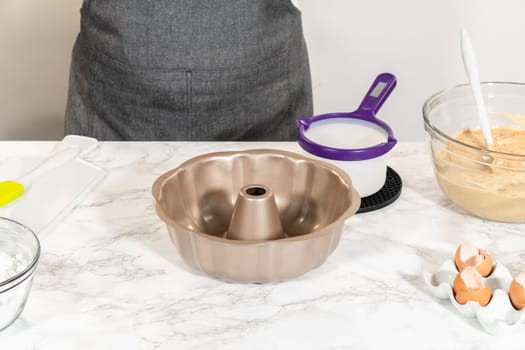 Using a silicone brush, the metal bundt cake pan is greased with melted vegetable shortening, preparing for baking the scrumptious Carrot Bundt Cake.