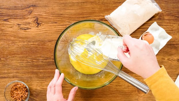 Flat lay. In a glass mixing bowl, a large hand whisk expertly blends the ingredients for a delectable gingerbread bundt cake with caramel frosting.