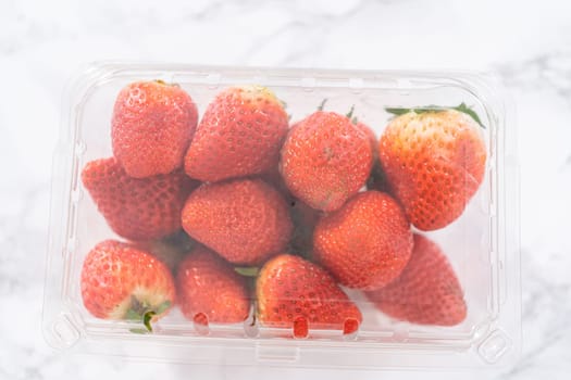 Fresh strawberries are showcased in their original store-bought plastic container, resting on a kitchen counter, ready to be washed, eaten, or stored.