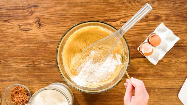 Flat lay. In a glass mixing bowl, a large hand whisk expertly blends the ingredients for a delectable gingerbread bundt cake with caramel frosting.