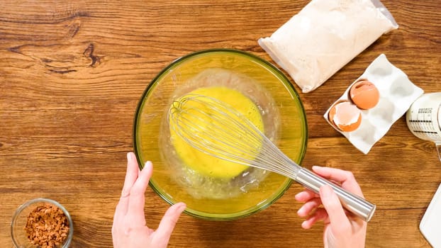Flat lay. In a glass mixing bowl, a large hand whisk expertly blends the ingredients for a delectable gingerbread bundt cake with caramel frosting.