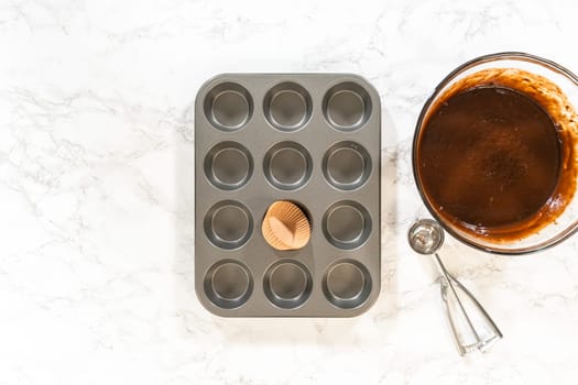 Flat lay. Getting ready to bake delicious chocolate cupcakes, we carefully line the cupcake pan with paper liners, ensuring a delightful treat awaits.