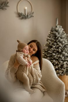 A woman holding a baby.The girl holds her child in her arms. The child is wearing a beige hand-knitted hat. mother and child are happy, they are smiling. They celebrate Christmas.