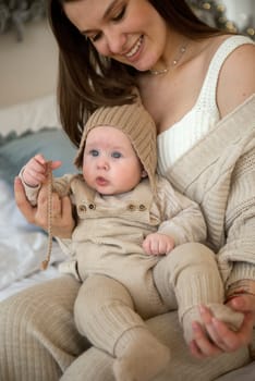 A woman holding a baby. High quality photo, The girl holds her child in her arms. The child is wearing a beige hand-knitted hat. mother and child are happy, they are smiling