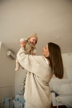 A woman holding a baby.The girl holds her child in her arms. The child is wearing a beige hand-knitted hat. mother and child are happy, they are smiling. They celebrate Christmas.