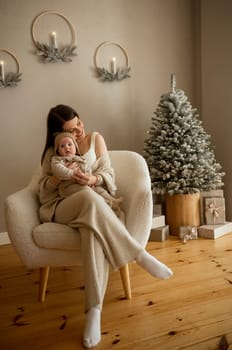 A woman holding a baby.The girl holds her child in her arms. The child is wearing a beige hand-knitted hat. mother and child are happy, they are smiling. They celebrate Christmas.