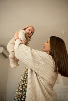 A woman holding a baby.The girl holds her child in her arms. The child is wearing a beige hand-knitted hat. mother and child are happy, they are smiling. They celebrate Christmas.