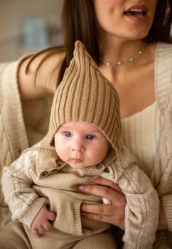 A woman holding a baby. High quality photo, The girl holds her child in her arms. The child is wearing a beige hand-knitted hat. mother and child are happy, they are smiling
