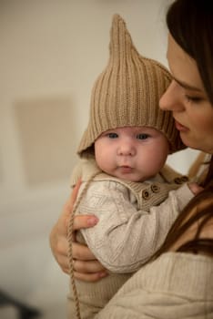 A woman holding a baby. High quality photo, The girl holds her child in her arms. The child is wearing a beige hand-knitted hat. mother and child are happy, they are smiling