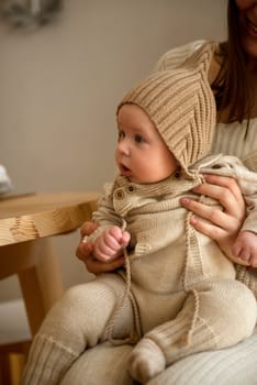 A woman holding a baby. High quality photo, The girl holds her child in her arms. The child is wearing a beige hand-knitted hat. mother and child are happy, they are smiling