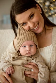 A woman holding a baby. High quality photo, The girl holds her child in her arms. The child is wearing a beige hand-knitted hat. mother and child are happy, they are smiling