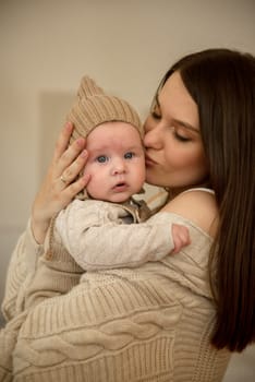 A woman holding a baby. High quality photo, The girl holds her child in her arms. The child is wearing a beige hand-knitted hat. mother and child are happy, they are smiling