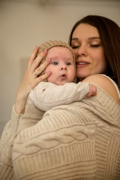 A woman holding a baby. High quality photo, The girl holds her child in her arms. The child is wearing a beige hand-knitted hat. mother and child are happy, they are smiling