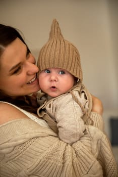 A woman holding a baby. High quality photo, The girl holds her child in her arms. The child is wearing a beige hand-knitted hat. mother and child are happy, they are smiling