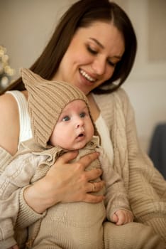 A woman holding a baby. High quality photo, The girl holds her child in her arms. The child is wearing a beige hand-knitted hat. mother and child are happy, they are smiling