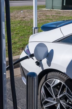 Modern electric car connected to DC high speed charger at public commercial facility for recharging battery