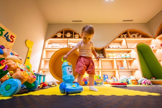 Toddler playing with a toy vacuum cleaner in a colorful and organized playroom for fun and learning