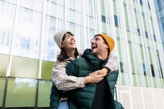 Man giving piggyback ride to woman in urban setting, both laughing and enjoying each other's company