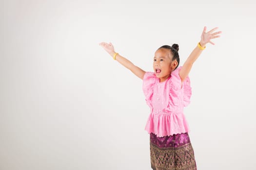 Portrait Thailand kid girl smiling traditional Thai dress costume raises fists in celebration of her success, studio isolated white background, kindergarten child saying yes with excitement winning