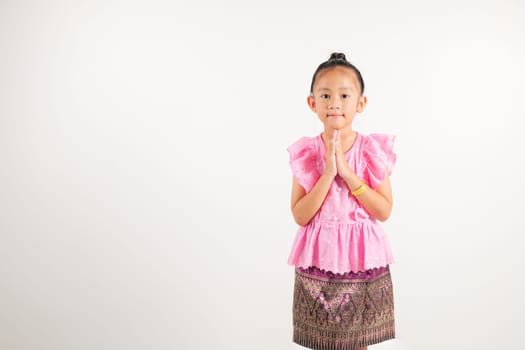 Portrait of Thailand kid girl smiling traditional Thai dress costume posing to pay respect in studio shot isolated white background, Happy kindergarten child sawasdee symbol or welcome