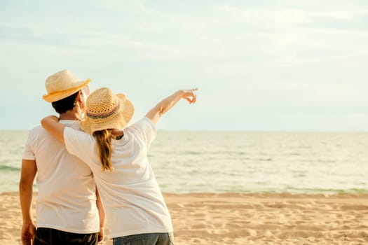 Back Asian couple standing hugging together on the beach, Happy young woman embracing her boyfriend seaside honeymoon vacation background, couple in love resting pointing on sea