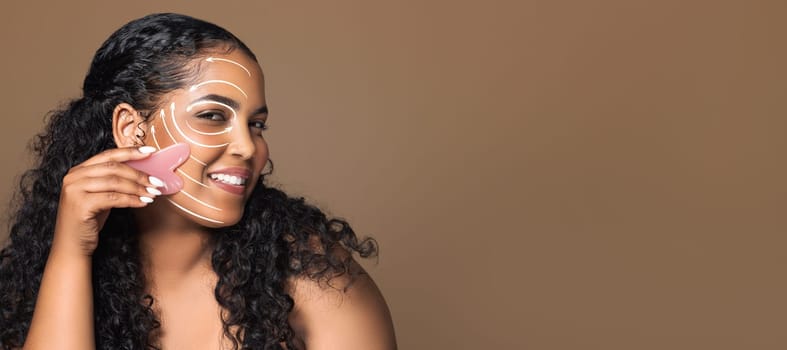 A woman enjoys her beauty routine, using a tool to apply skin care treatment on her smiling face. She is isolated against a soft brown background, emphasizing her relaxation.