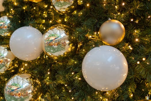 Closeup of shiny golden baubles hanging on illuminated Christmas tree at home. Full frame shot of ball decorations during Xmas eve