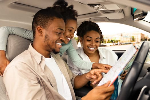 Road Trip Adventure. Happy African American Family Holding Map Sitting In Car Choosing Destination For Vacation. Travel By Automobile. Transportation And Navigation. Selective Focus, Side View